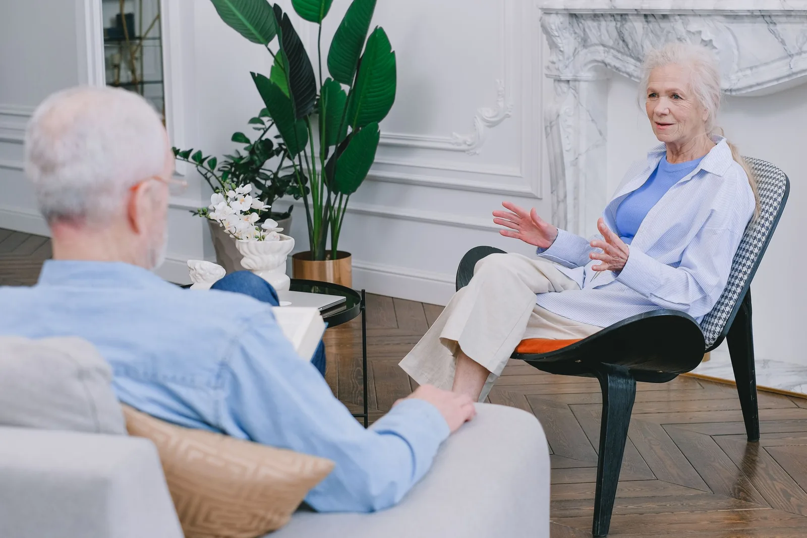 A woman and man seated facing each other in a bright living room.