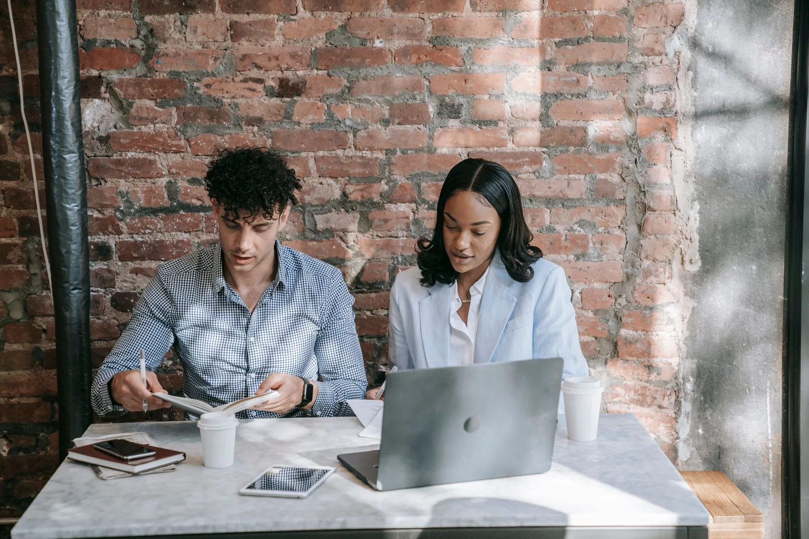 Two people reviewing notes together beside an open laptop.