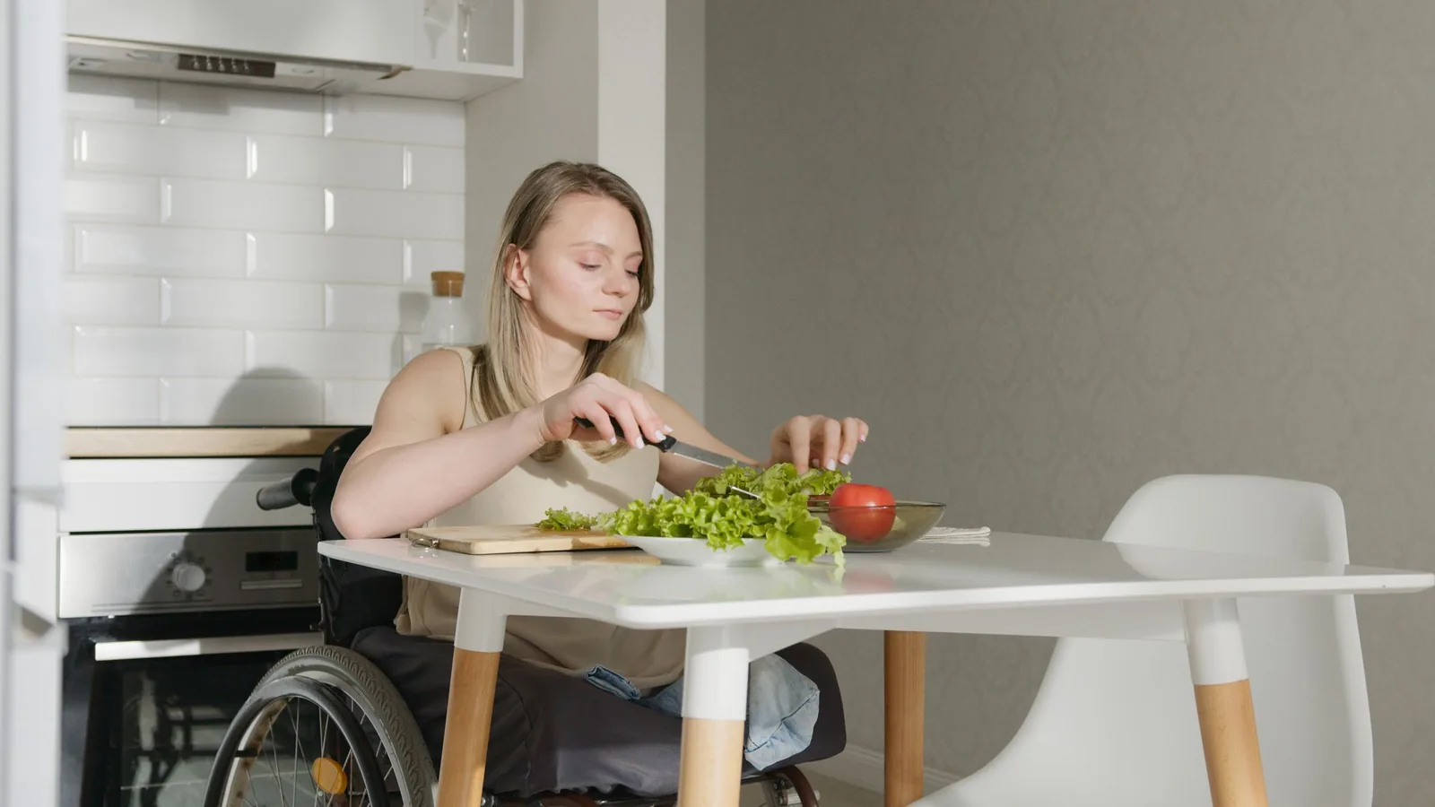 A woman using a wheelchair preparing vegetables at a kitchen table.