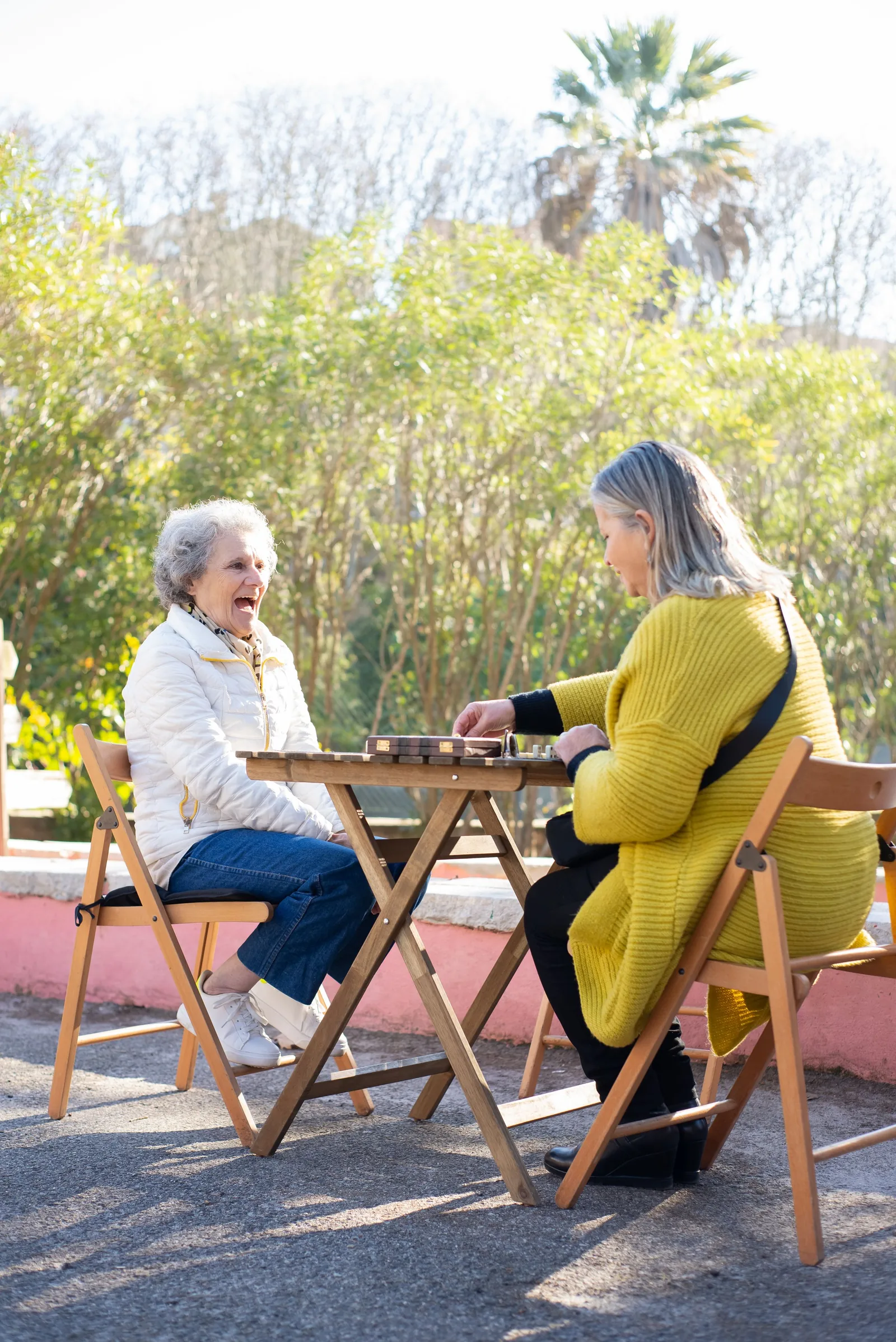 Two women smiling together over a table game outdoors.