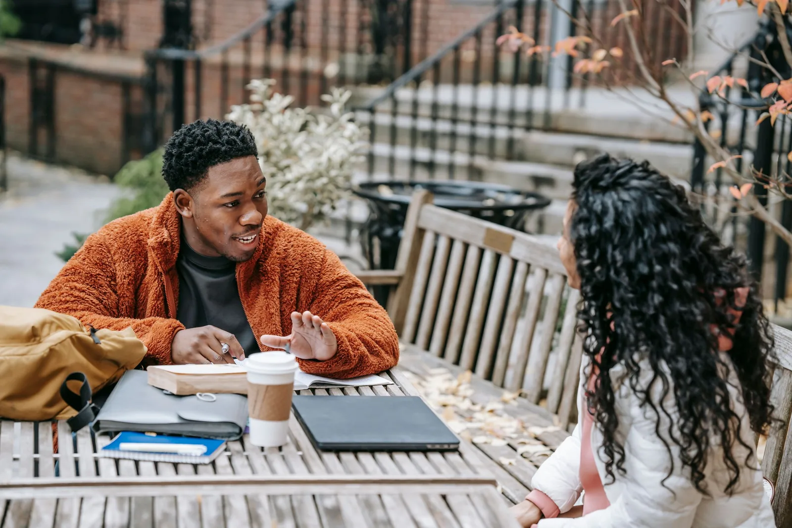 Two people discussing their work at an outdoor table with a laptop and notebooks.