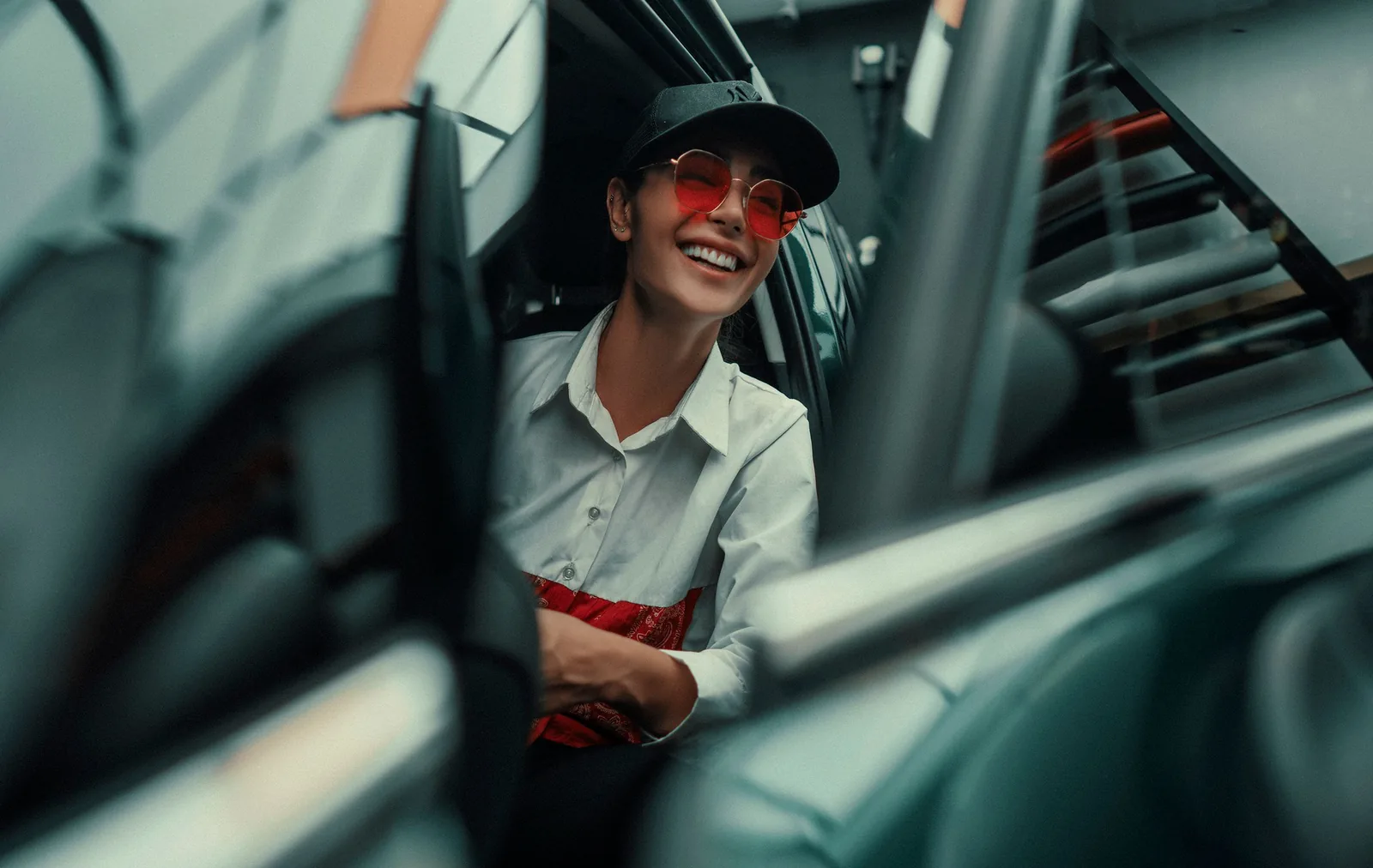 A smiling woman wearing sunglasses seated in a car.